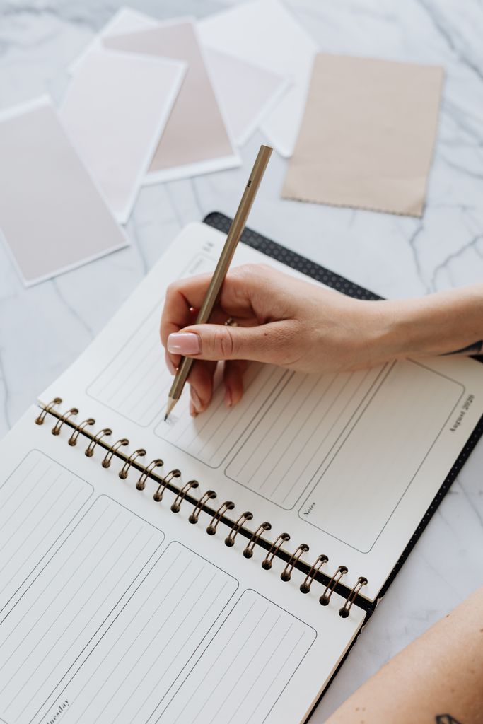 Close-up shot of a hand writing in a spiral notebook on a marble table with color swatches.